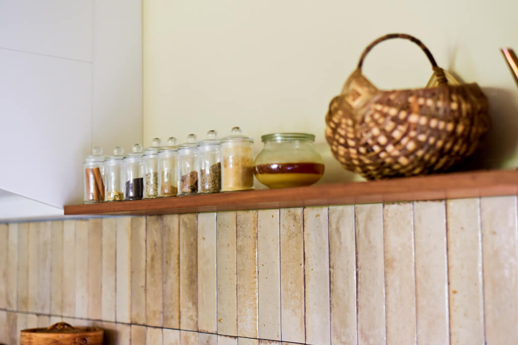 質感のある縦長タイルと、スパイスボトルが並ぶおしゃれな木製オープンシェルフ。