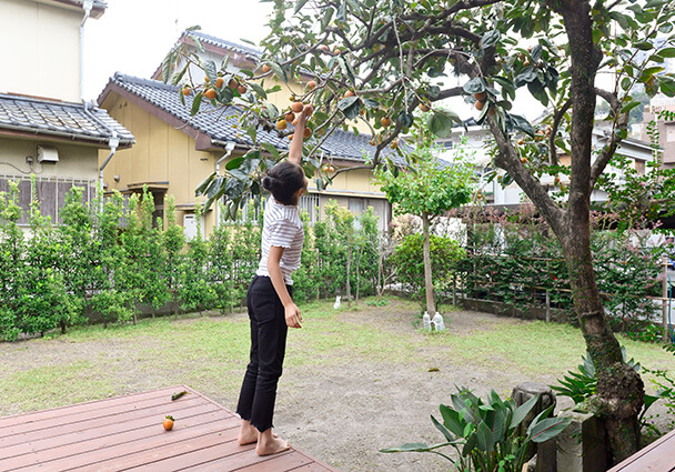 庭の柿の木を残し、住み継ぐ家の暮らしを楽しむ家族。ウッドデッキと庭