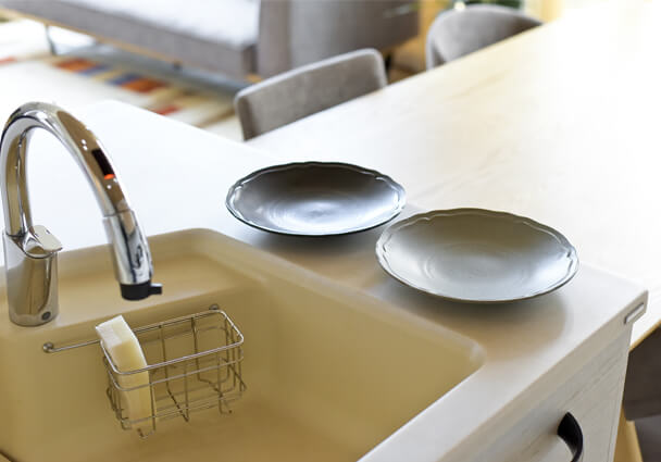 2列型キッチンのアイランドシンク周り。水栓とシンプルなスポンジラック、陶器の皿。