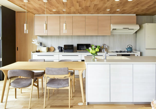 LDKと一体感のある2列型キッチンの全景。木目調の天井とダイニングテーブルがおしゃれな空間。