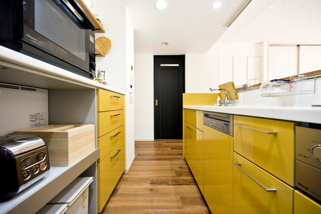 黄色のキッチンカウンターと黒い建具のコントラストが美しい、モダンで温かみのあるキッチンのレイアウト。