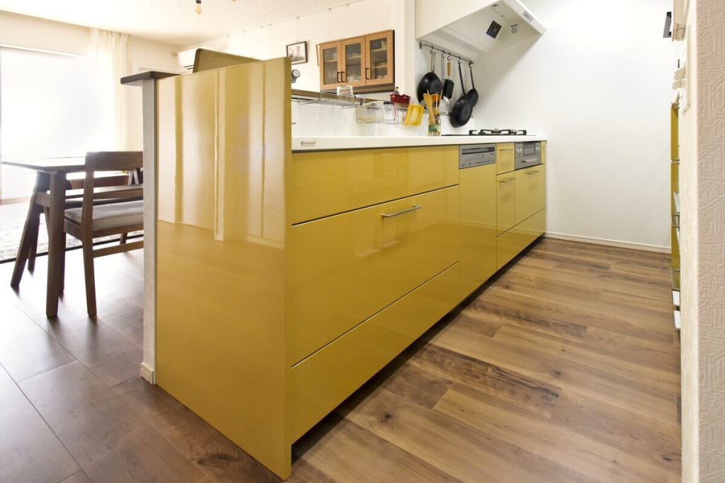 トクラスの黄色いキッチン（深支子色）のサイドパネルが見える全体像。人造大理石カウンターと、ミーレの食洗機、リンナイのコンロがビルトインされている。フルリノベーションマンションのLDKに設置。