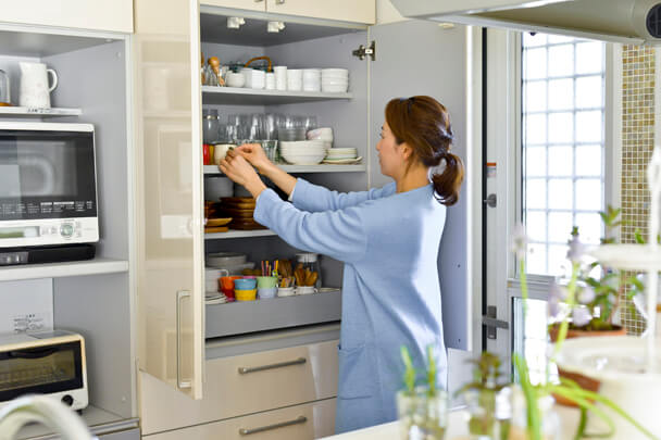 家族みんなが使いやすいよう整理整頓された食器棚と、食器をしまう女性