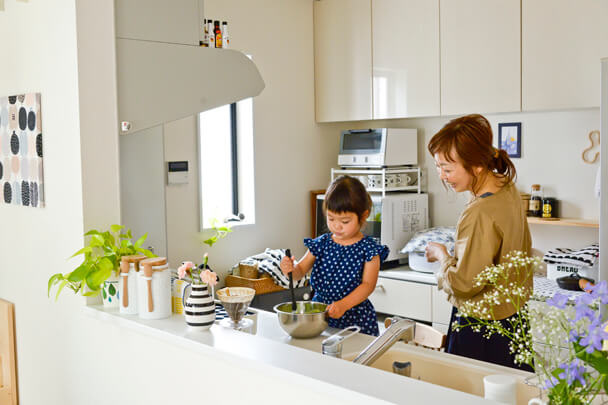 ママと一緒にキッチンでお手伝いクッキングを楽しむ娘さん。親子の笑顔。