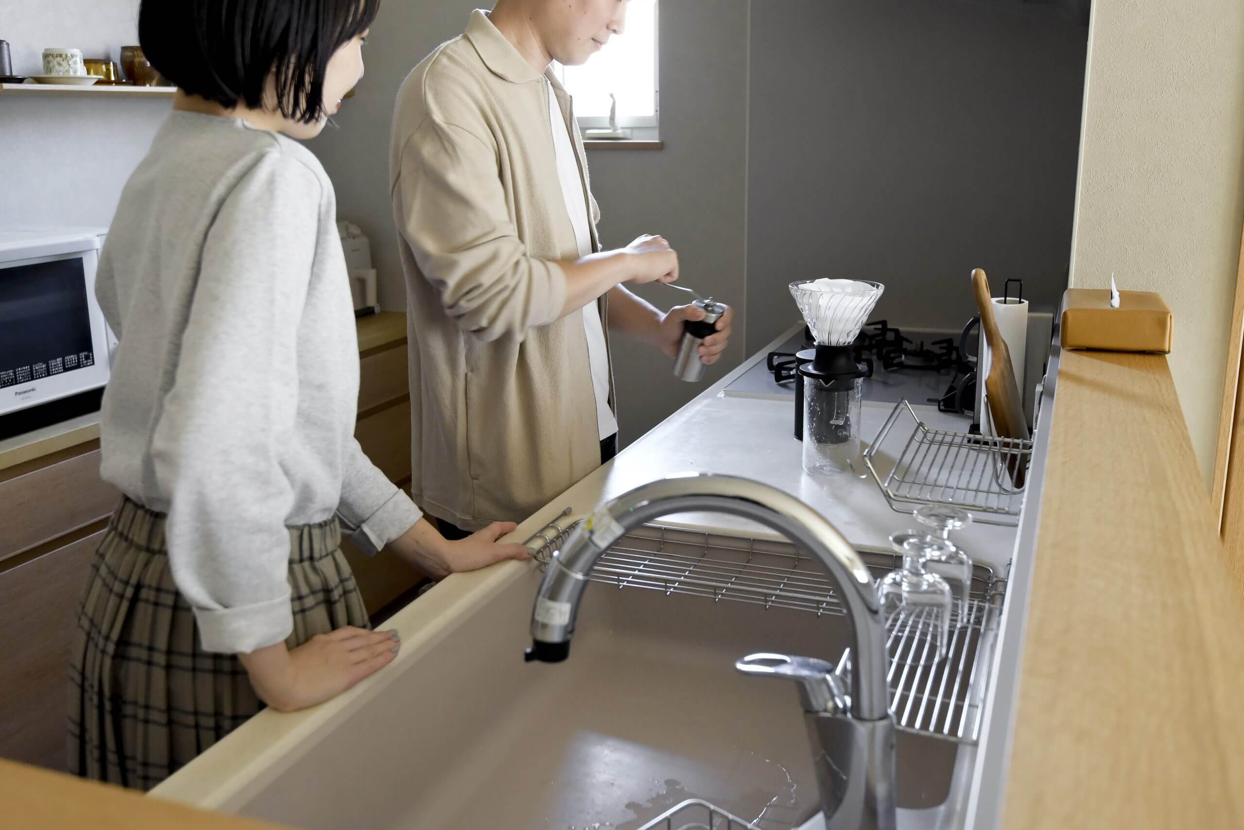 和モダンなキッチンカウンターで夫婦がコーヒー豆を挽く様子。心地よい光が差し込む空間での、朝の生活風景。