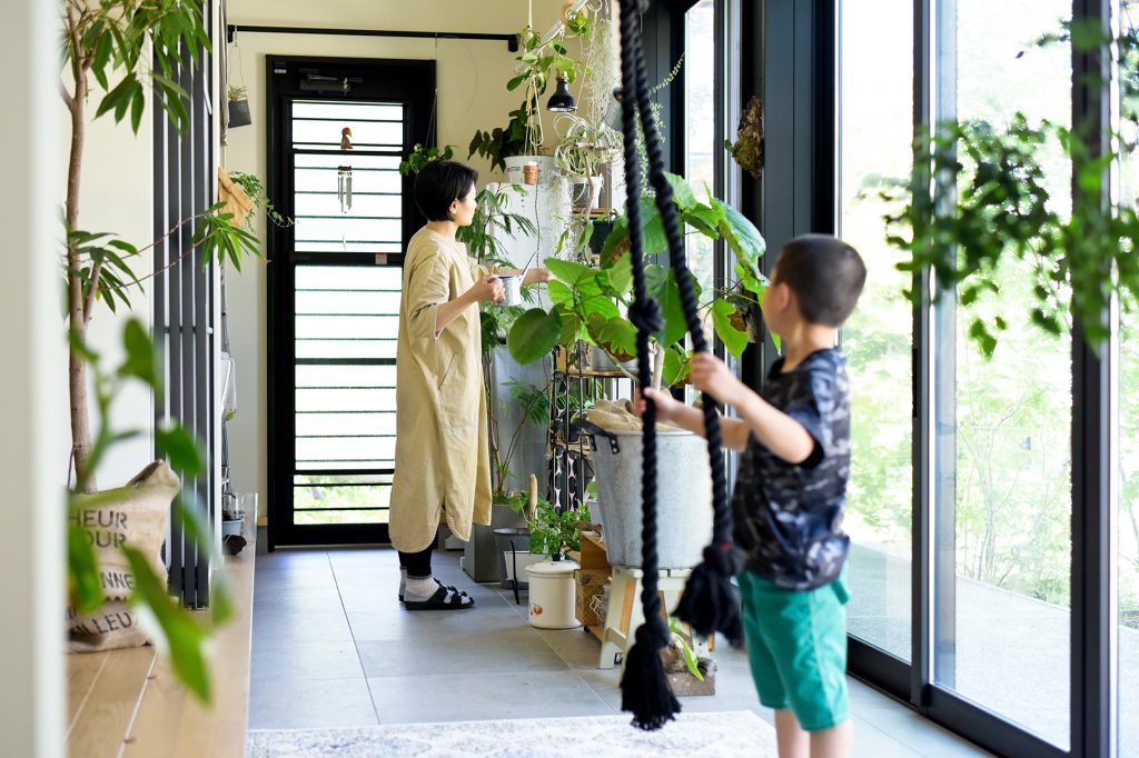 庭をインテリアの主役にした土間玄関。大きな窓から植物を眺める家族の暮らし。