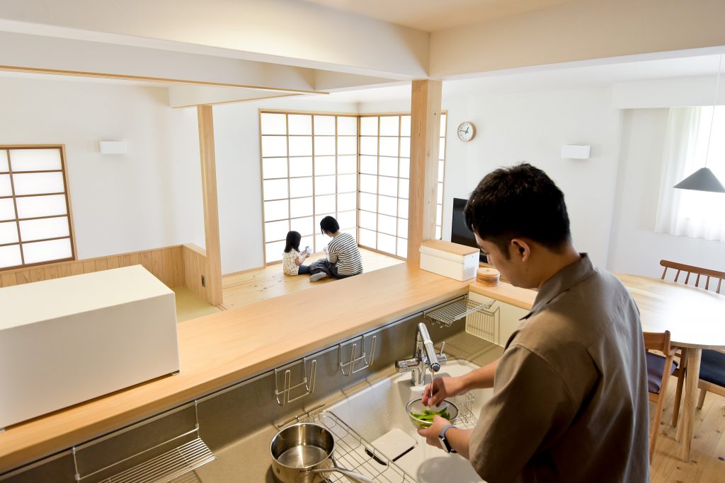 和モダンな住まい。父親がキッチンで料理し、子供たちが遊ぶ家族の風景。