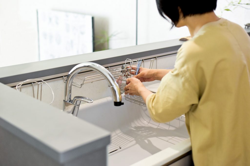 家事効率を考えたワイドシンクと水栓。水切りカゴを設置する女性の手元。
