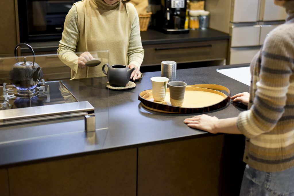 親子世帯がキッチンで一緒にお茶の準備をする様子。和の急須や湯呑みが、落ち着いた空間での団らんを演出。
