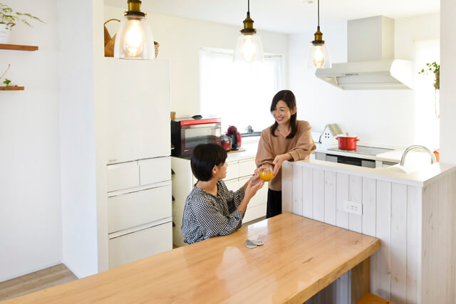 U型キッチンのカウンター越しに子供と会話する母親。機能的な設計で家事をしながらコミュニケーションが取れる。